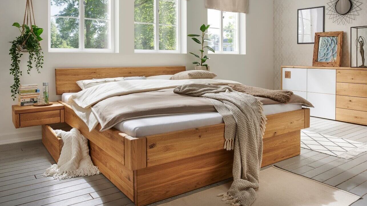 Holzbett in einem hellen Schlafzimmer mit gro&szlig;en Fenstern und nat&uuml;rlichen Materialien