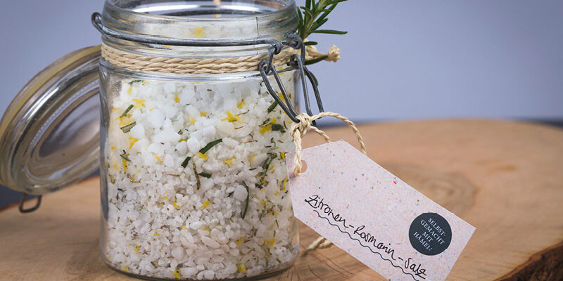 Glas mit selbstgemachtem Rosmarin-Zitronen-Salz, frische Kräuter und Zitrone sichtbar