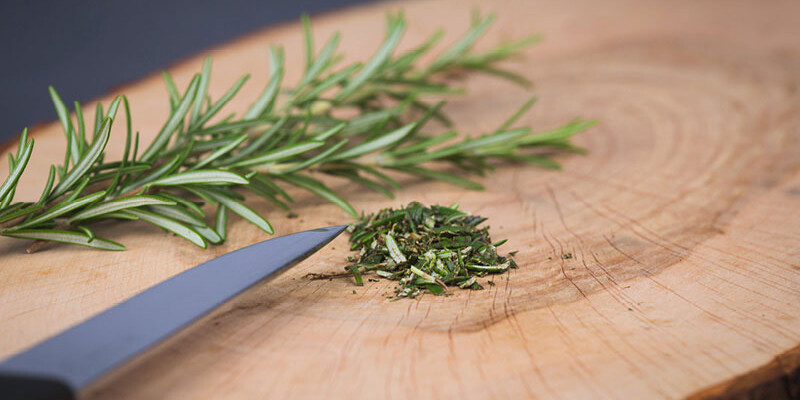 Frisch gehackter Rosmarin auf Holzbrett mit Messerspitze“