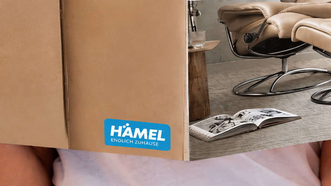 H&auml;nde halten einen M&ouml;belkatalog mit H&auml;mel Logo