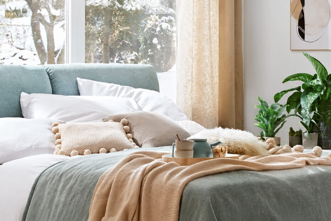 Helles Schlafzimmer mit gepolstertem Bett, Textilien und gr&uuml;nen Pflanzen